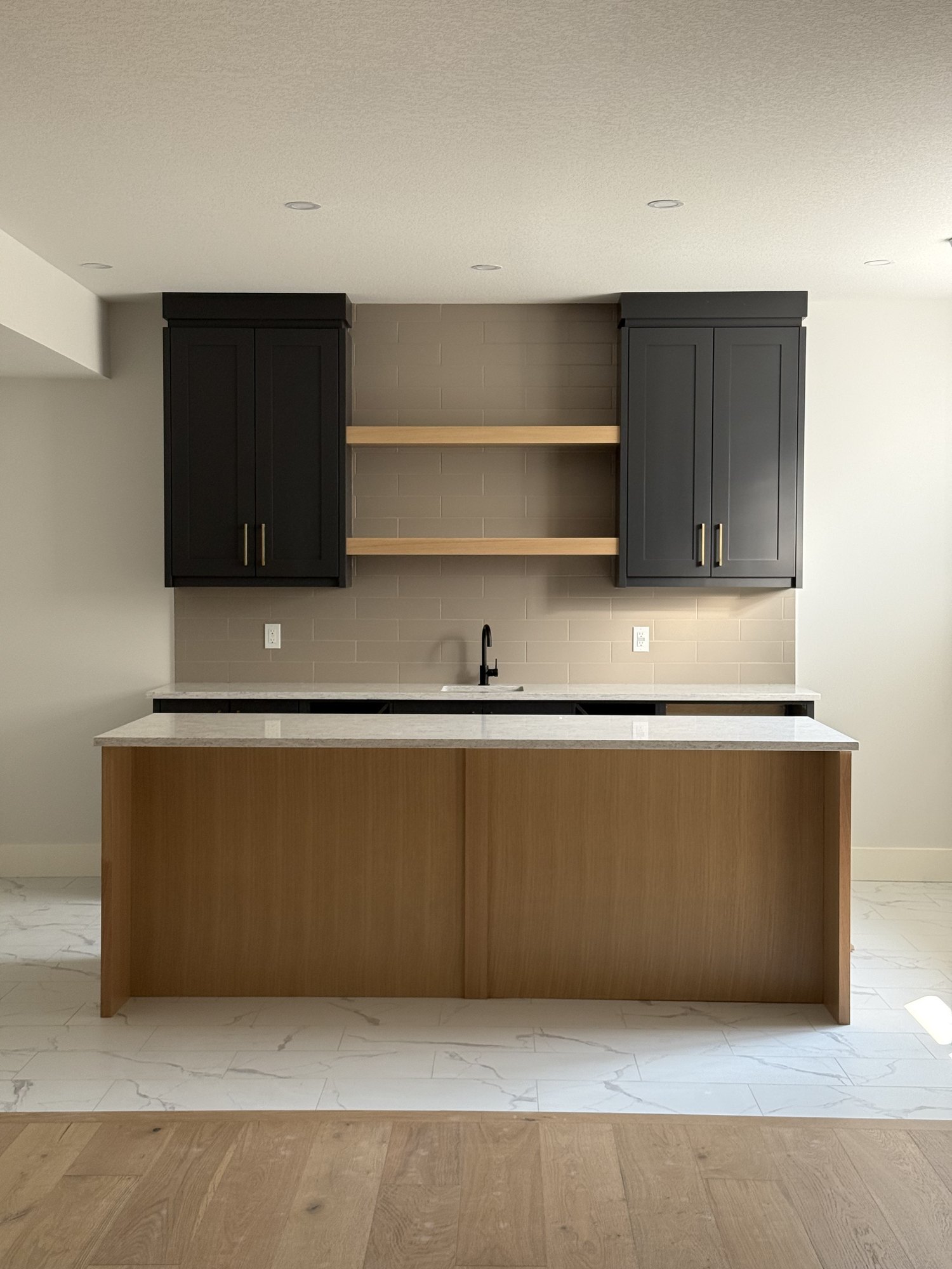 Wet bar with an oak island, black upper cabinets and oak floating shelves