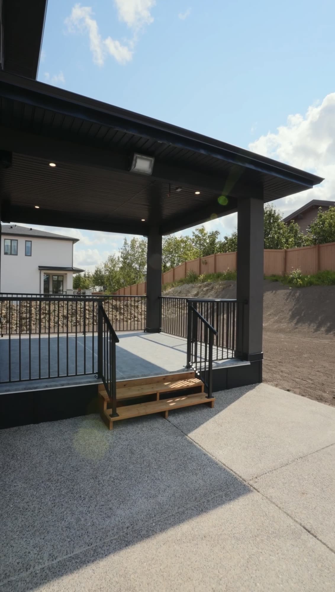 Covered rear deck with a black railing and a concrete patio below