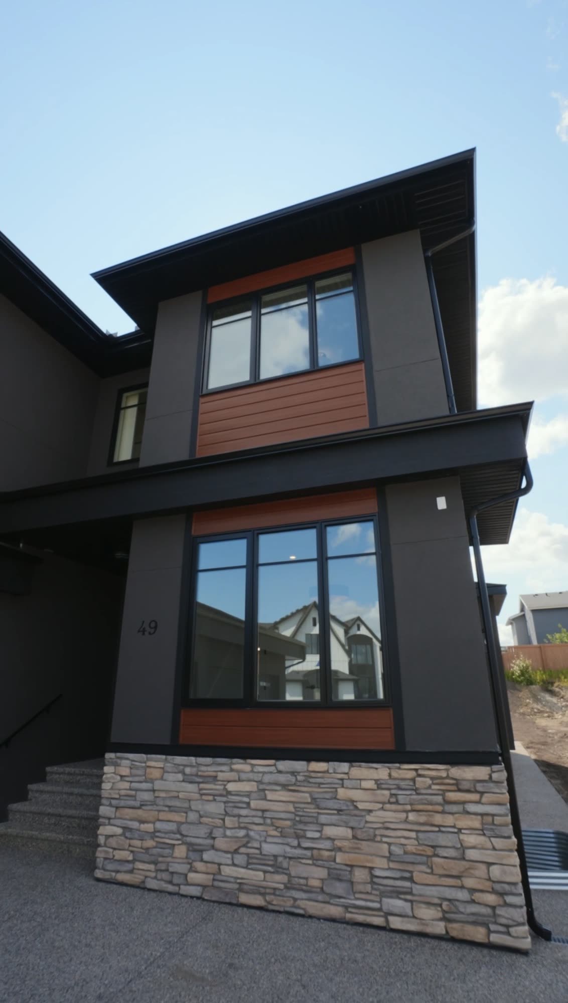 Front elevation in dark siding with a cedar toned accent panel over a stone base