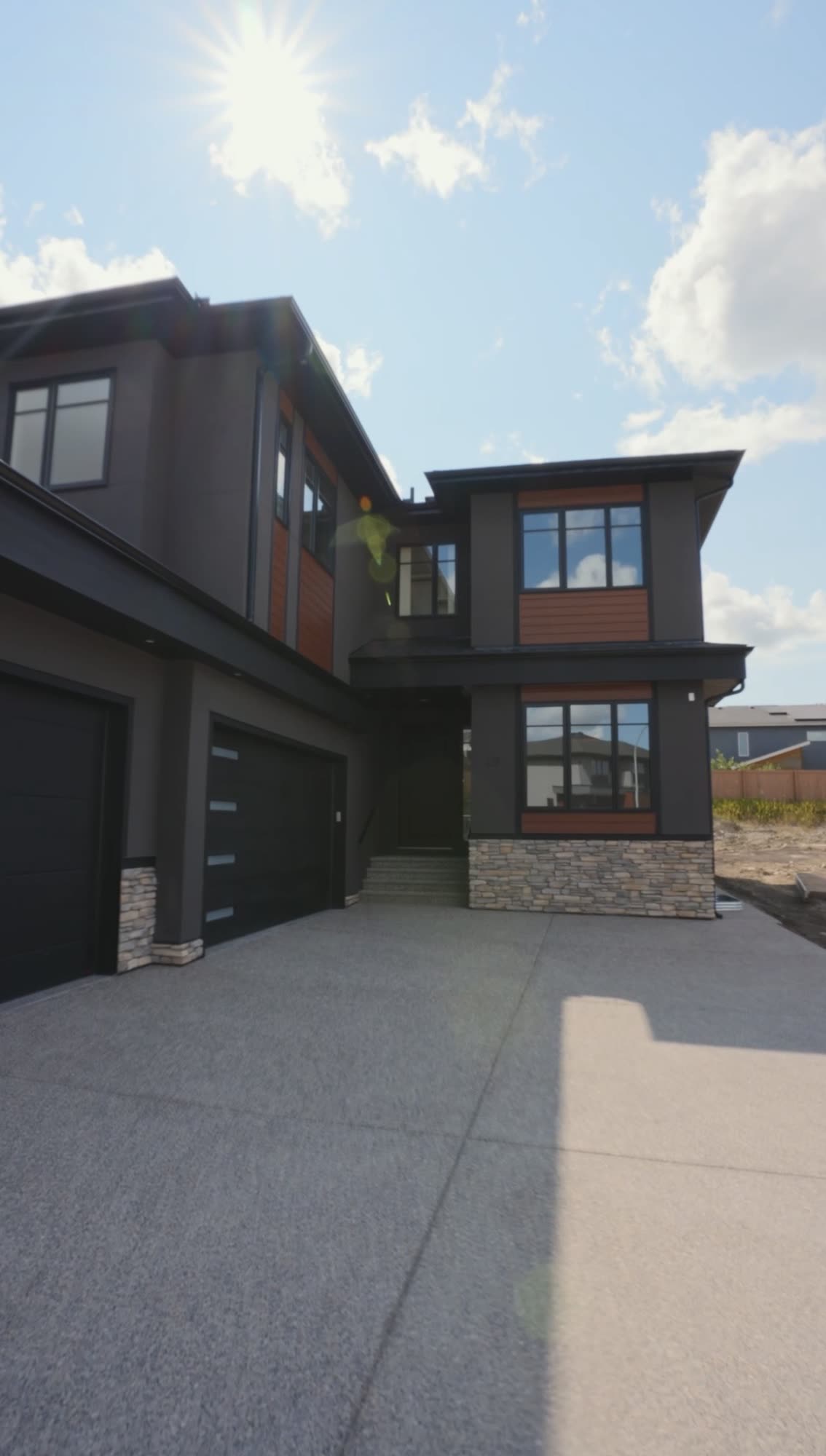 Front of a finished home in dark siding with the garage and driveway