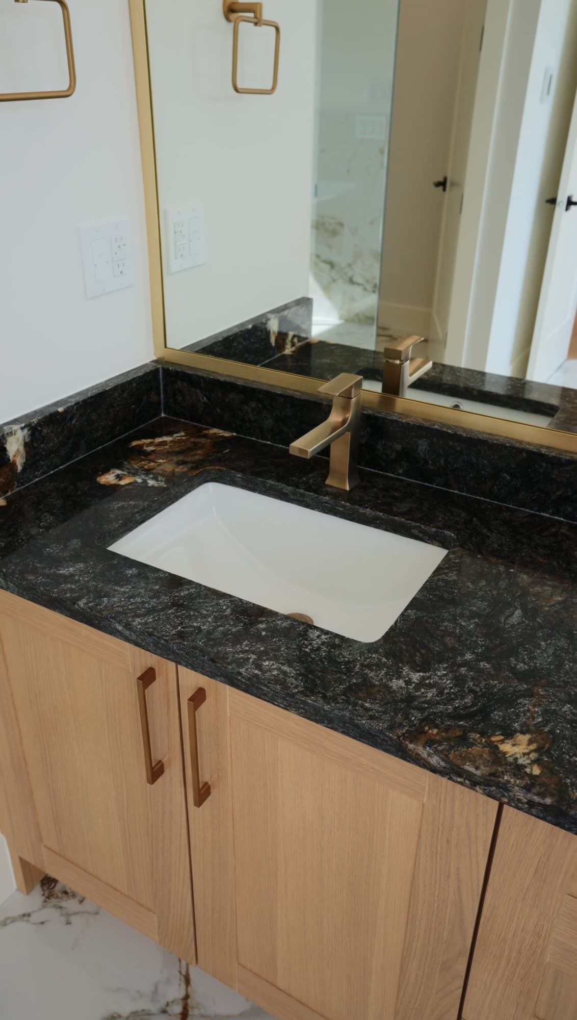 Vanity with an oak cabinet, a black granite counter and a brass tap