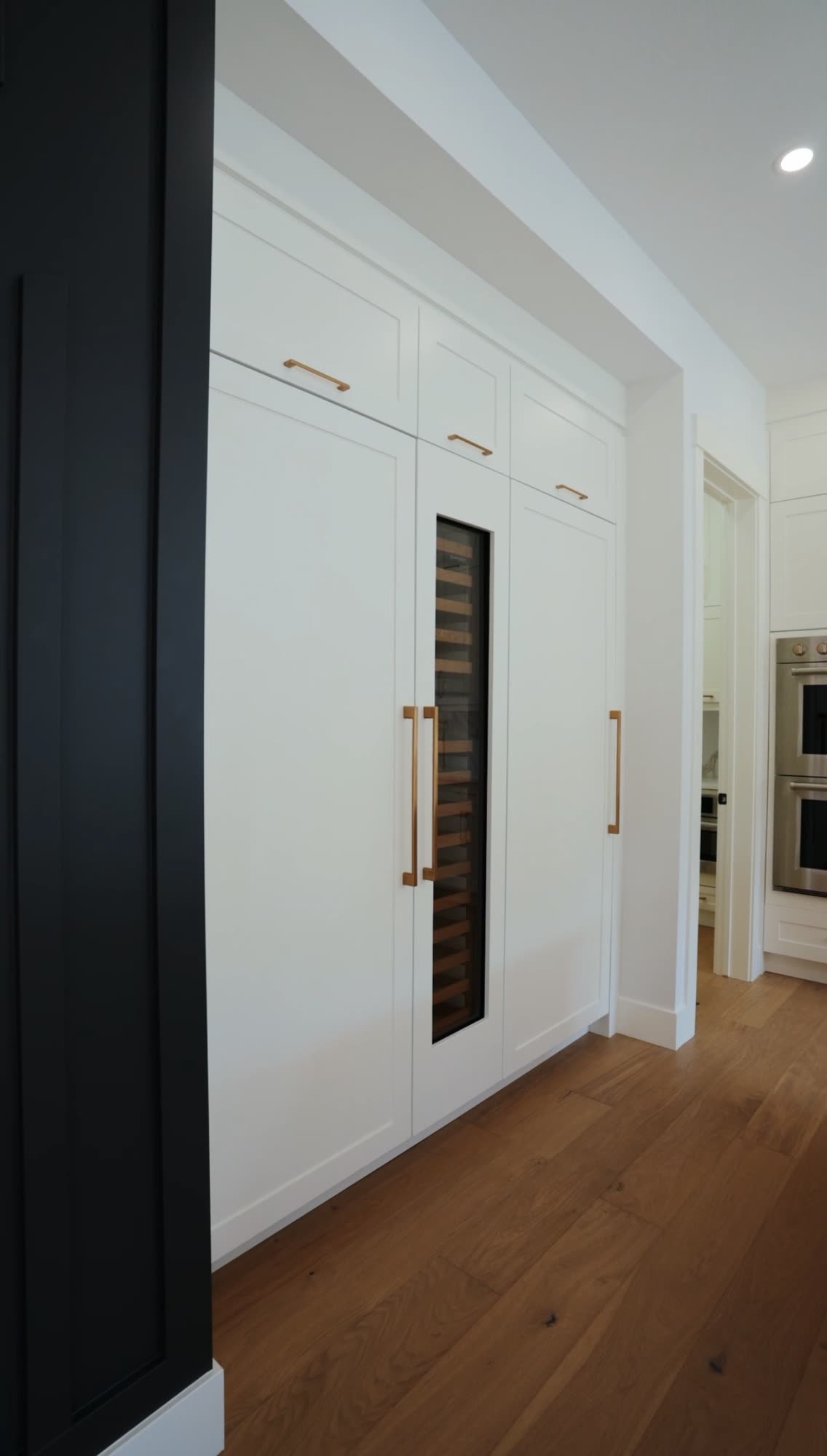 Black millwork with a glass fronted wine fridge beside white pantry doors