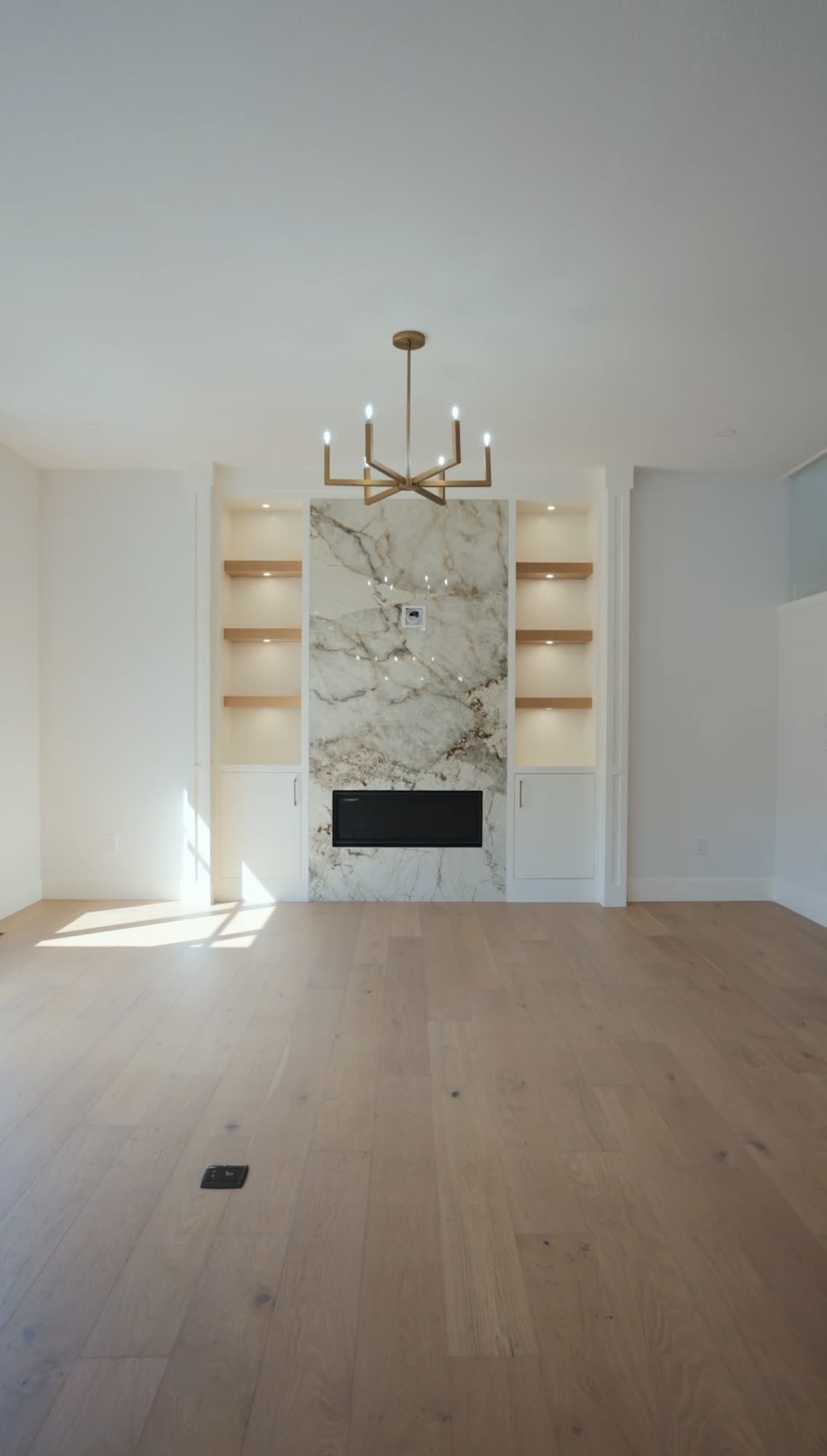 Marble fireplace wall with oak shelving and a chandelier over an oak floor