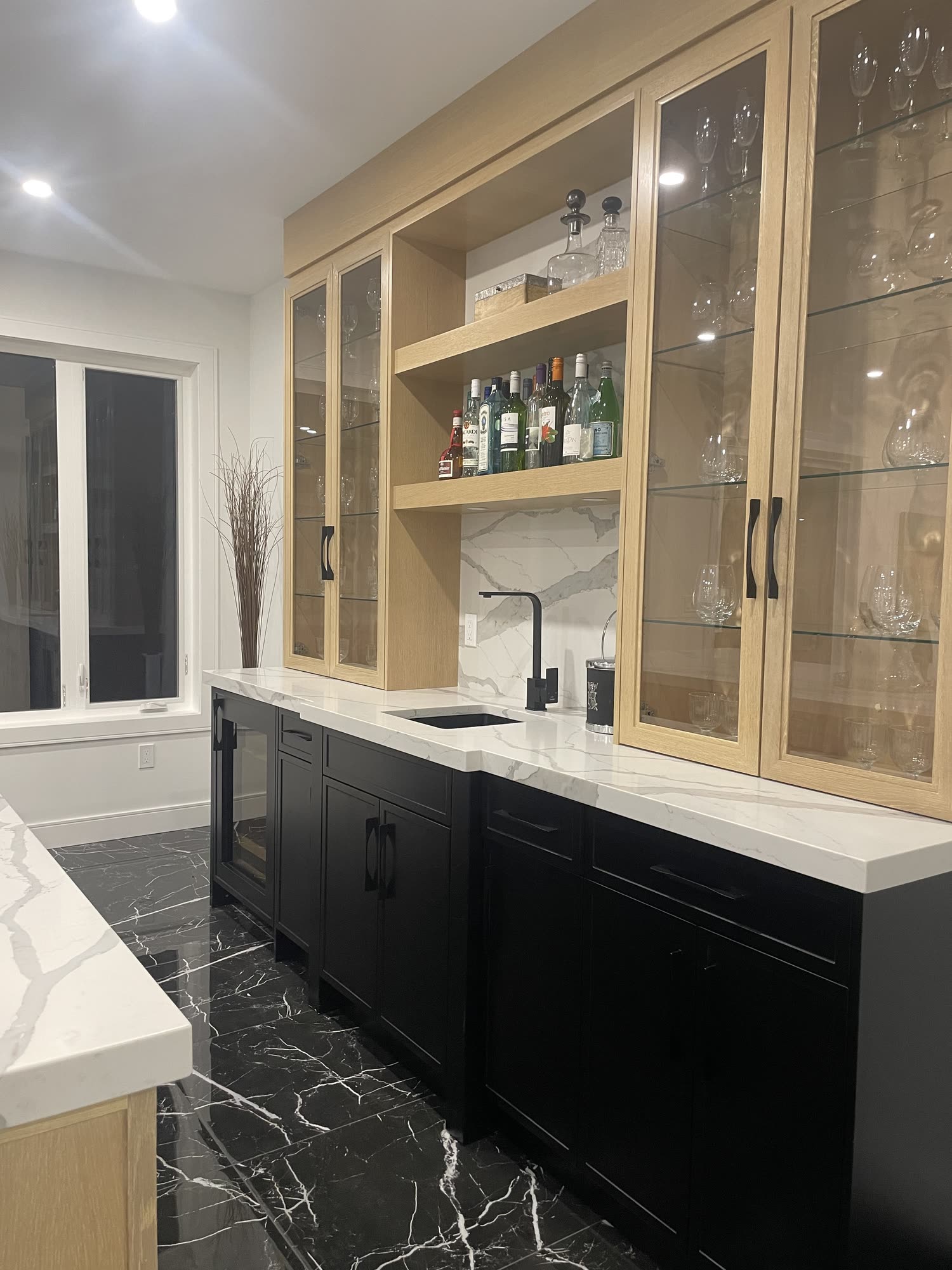 Bar with glass fronted oak cabinets, black lower cabinetry and a marble floor
